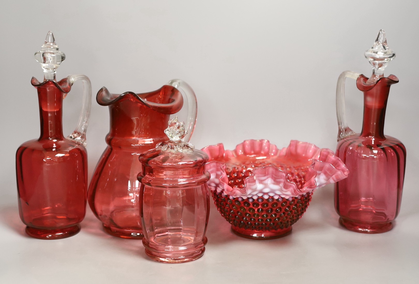 A pair of cranberry glass decanters, a jug, a fluted vase and a biscuit box and cover- decanters and stoppers 28cms high.